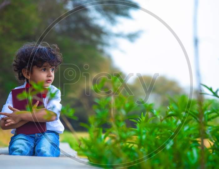 Sad Boy Sitting In Park With Holding Book In His Hand.