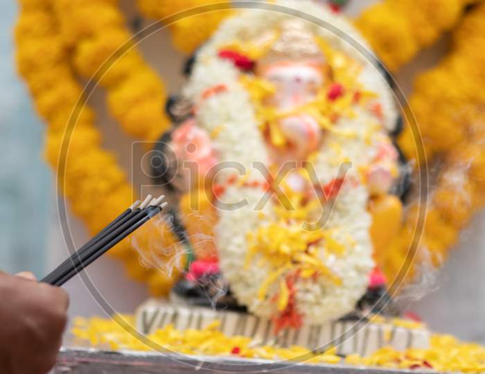 Hands Holding Or Offering Incense Or Agarbatti Stick In Front Of Lord Vinayaka Or Ganesha While Praying Or Worshiping During Festival Ceremony