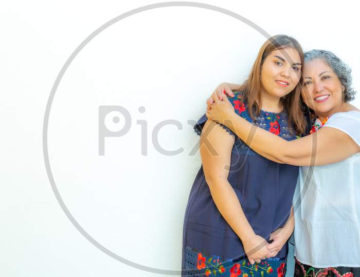 Mother Hugging Her Daughter With A Lot Of Love, Two Smiling Mexican Women On A White Background, Space For Text