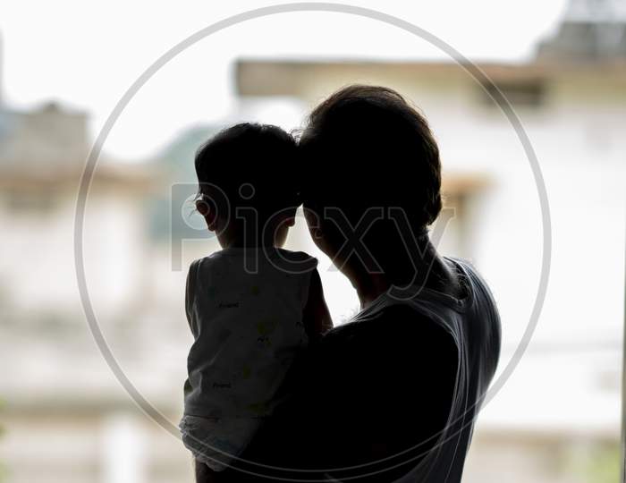 Silhouette of a father holding his child in his arms and looking outside the window
