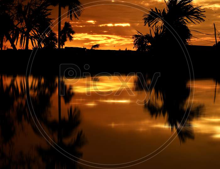 Beautiful Landscape of Illuminated Colorful Sky at Sunset, Reflection on Lake Water After Rain in Afternoon. All Are Black in Shadow And Bright Yellow Clouds on The Sky by The Last Sunshine of Day.