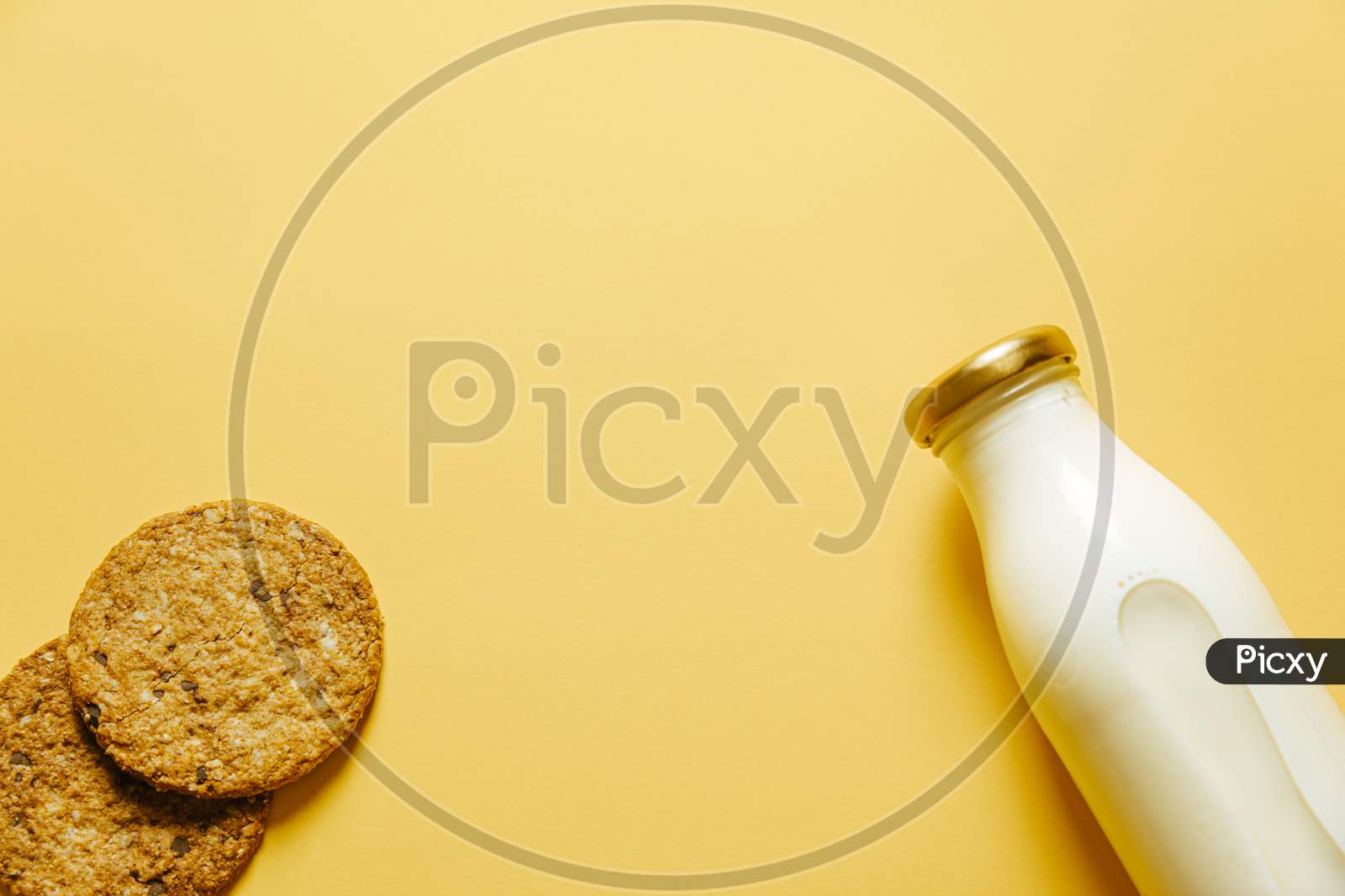 Two Cookies And A Bottle Of Milk Over A Yellow Wallpaper