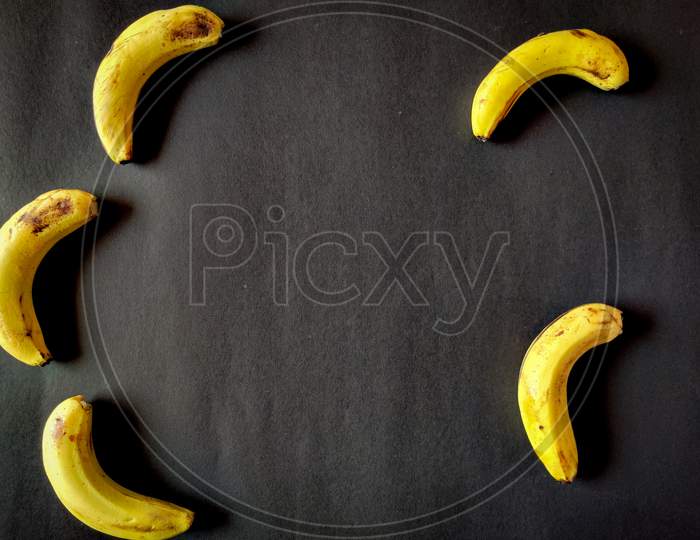 Five Bananas Isolated On Black Background. Copy Space In Center.