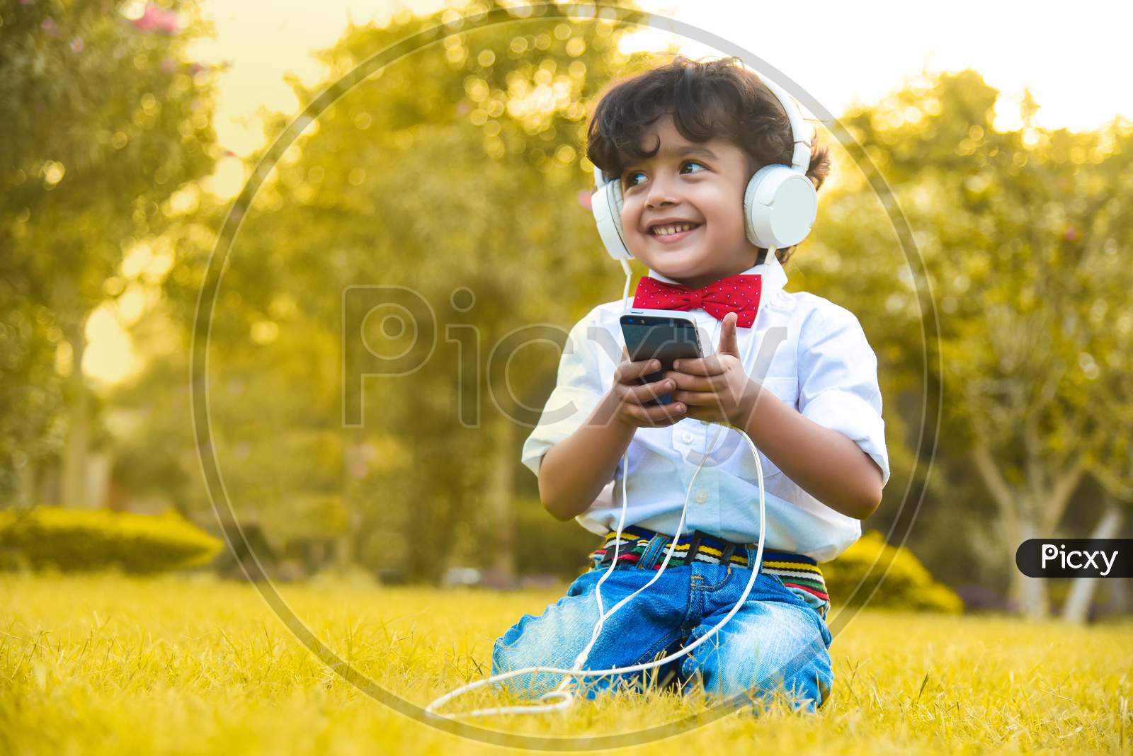 Little Boy Listening To Music From His Phone On His White Headphones.