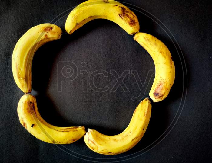 Five Bananas Isolated On Black Background. Copy Space In Center.