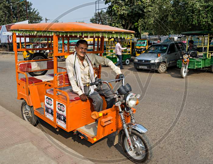 Driver Of Orange Battery Operated Electric Auto Rikshaw Waiting For Passengers.