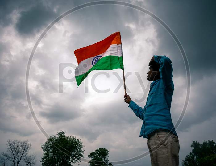 A boy holds and gives a salute to the indian flag or tricolour flag on the independence day under the clouds, 15 august 2020
