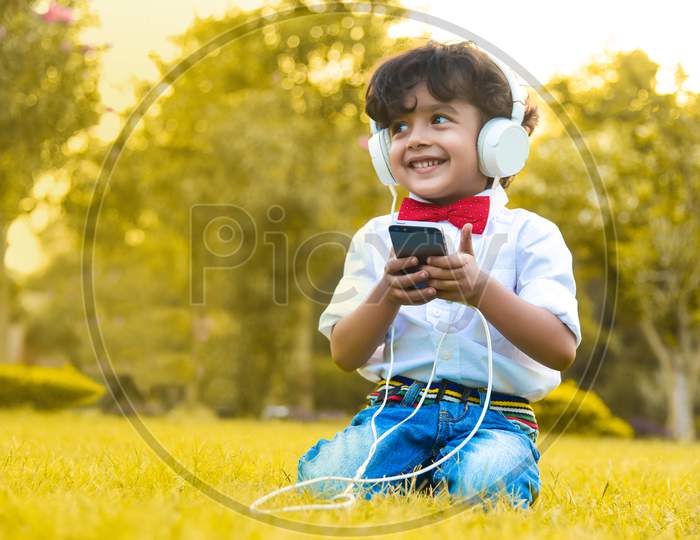 Little Boy Listening To Music From His Phone On His White Headphones.