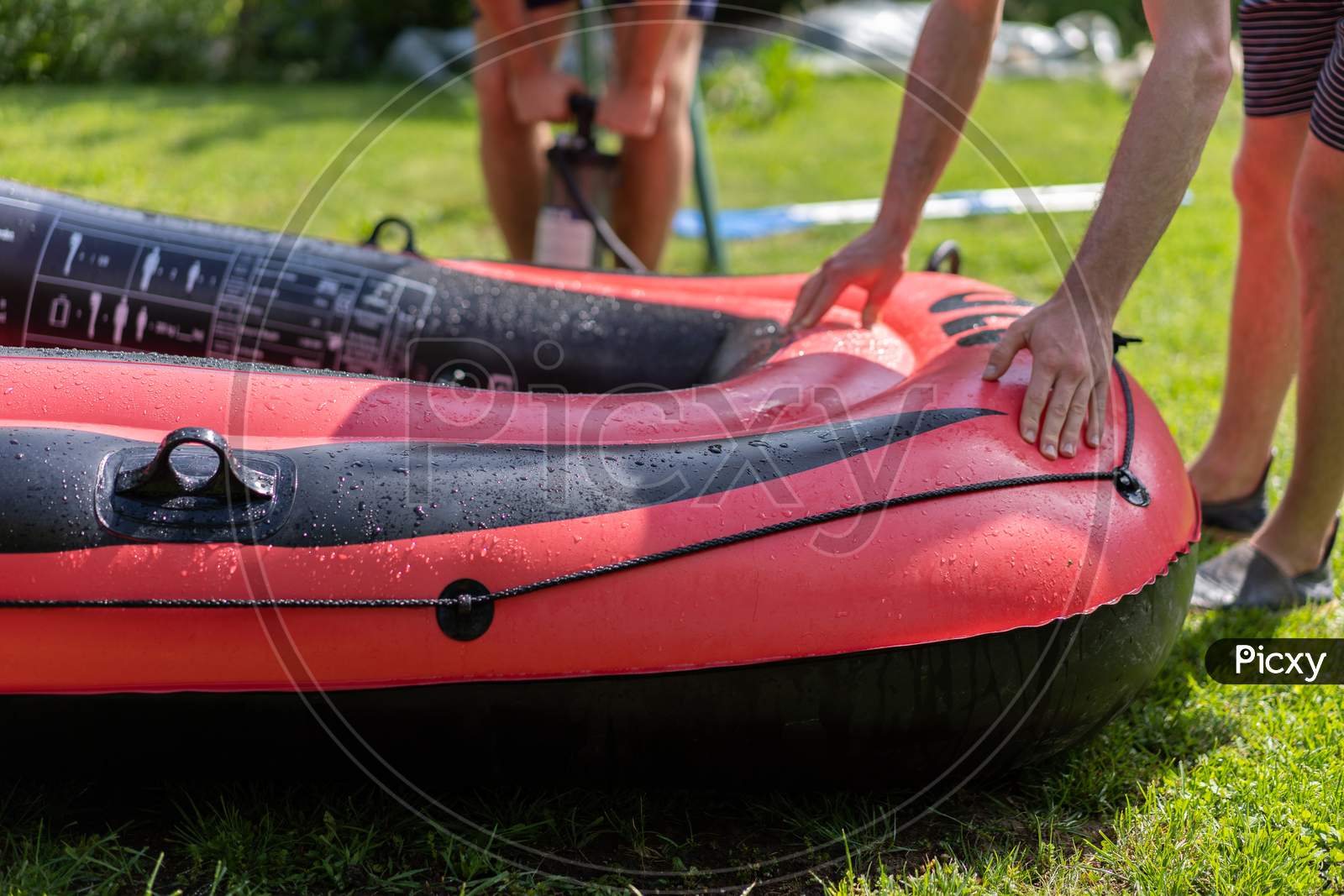 Close-Up Of Red Rubber Boat, Inflated With A Hand Pump And Checked By Two Young Men.