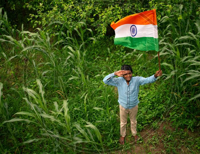 A boy holds and gives a salute to the indian flag or tricolour flag on the independence day at a farm, 15 august 2020