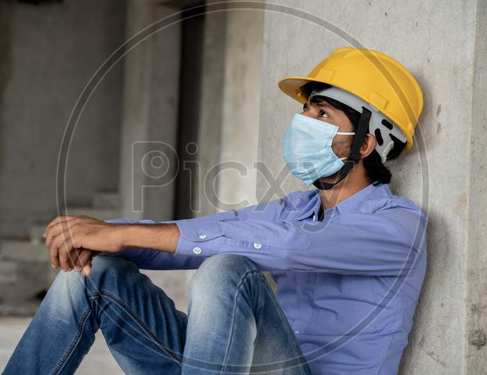 Head Shot Side View Of Construction Worker Seeing Outside From Construction Building Window In Sad - Industrial Worker In A Hardhat With Medical Mask Due To Coronavirus Or Covid-19 Crisis.