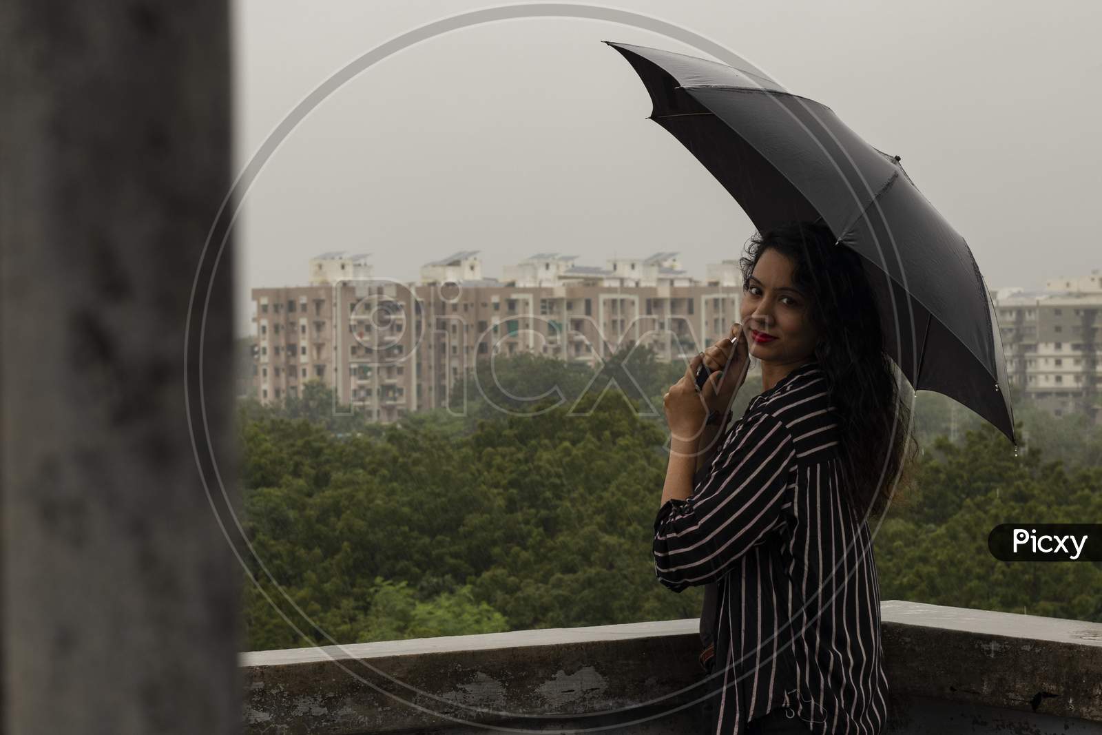 Indian Woman With Umbrella In The Rain. Looking At Camera.