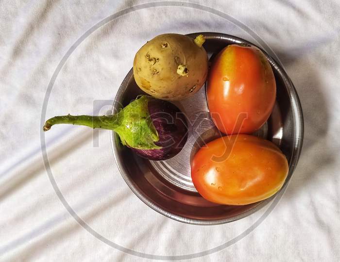 Vegetables tomatoes, brinjal and potato isolated in steel plate on silk white fabric with folds