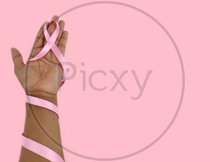 Pink ribbon breast cancer awareness symbol kept between hands as Support and care Concept