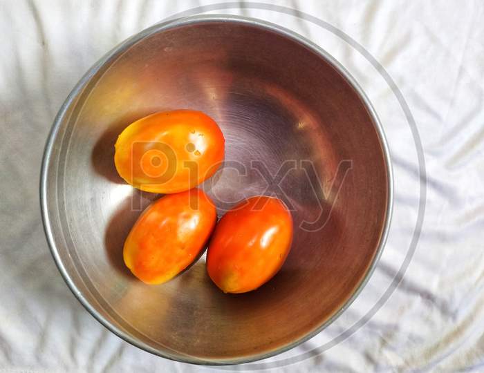 Three red tomatoes in hod pan on white background