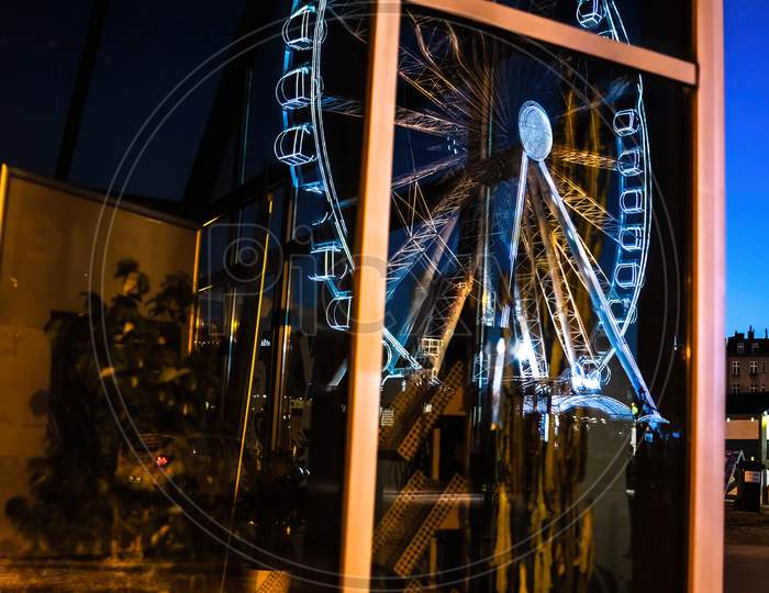An Abstract Image Containing Reflection Of A Ferries Wheel On A Glass House With Plants During Night Time Located In Gdansk City Of North Poland Near Baltic Sea