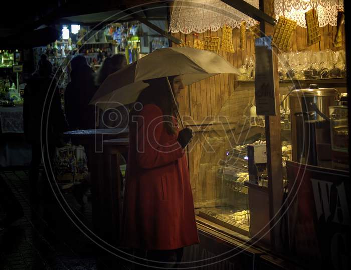Krakow, Poland - December 22, 2014: A Girl In Red Coat Holding Umbrella In Front Of Waffle Shop During Christmas Eve Holidays In City Center Main Square