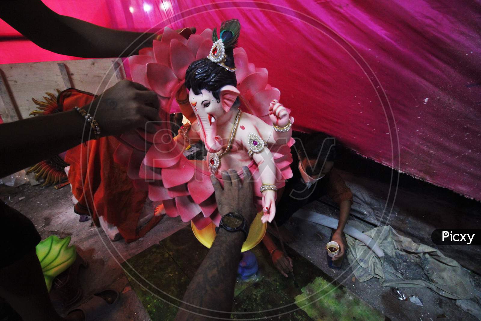 People set up the idol of Hindu God Ganesh, the deity of prosperity and a woman paints the base on which the ganpati is kept, before the start of the Ganesh Chaturthi festival in Mumbai, India on August 21, 2020.