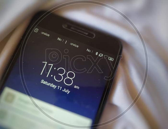 Time and date showing in smartphone rest on white silk cloth.