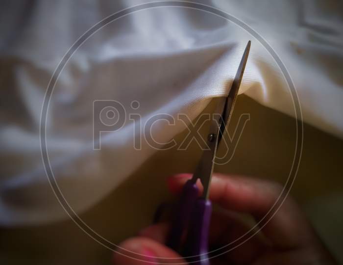 Cutting soft fabric by scissor held with hand.