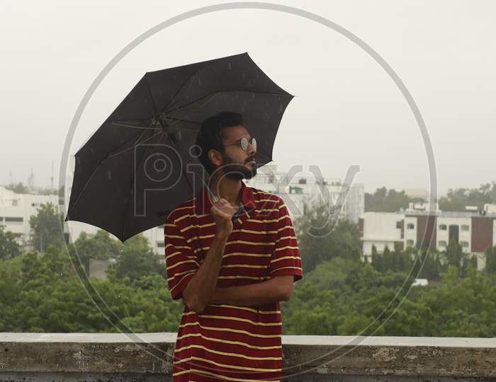 Indian Man Standing In Rain With Black Umbrella