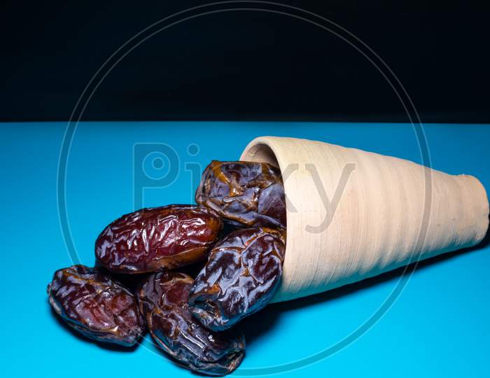 A Bunch Of Fresh Dates Spread From A Clay Pot With Blue Background
