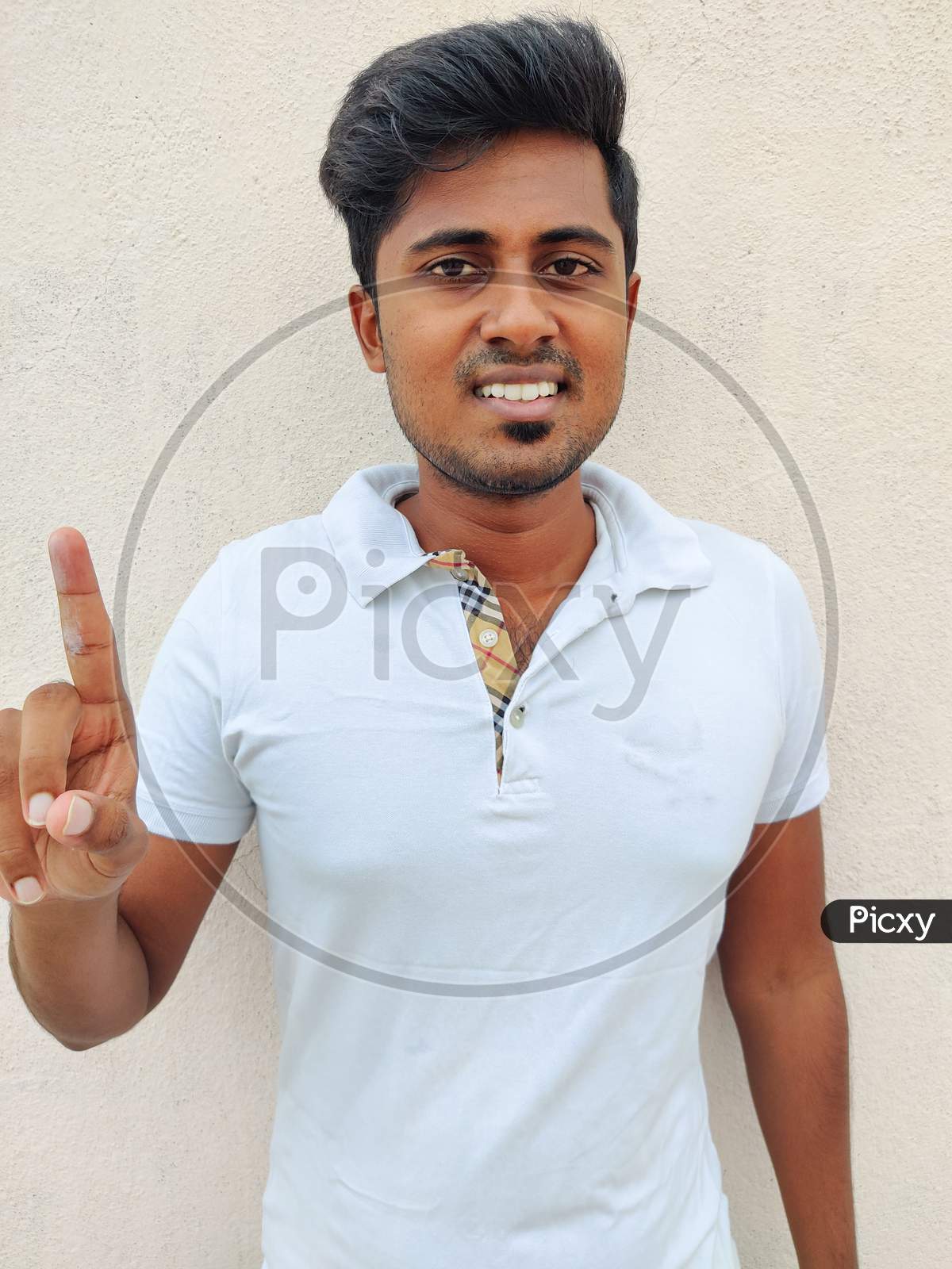 Smiling South Indian Young Man Wearing White Tshirt Pointing Up With Fingers Number One. Isolated On White Background.