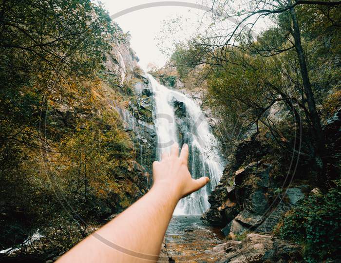 Horizontal Shot Of An Out Of Focus Hand Reaching A Massive Waterfall