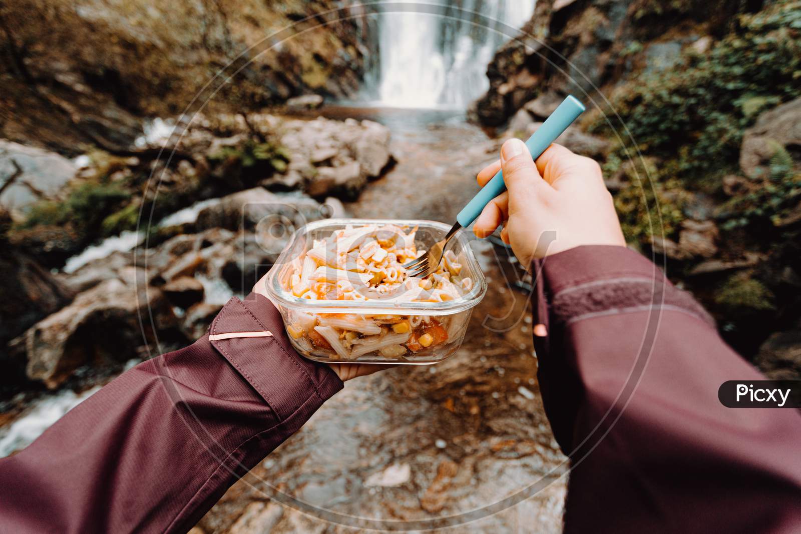 A Point Of View Shot Of A Female Hiker Eating In Front Of A Waterfall