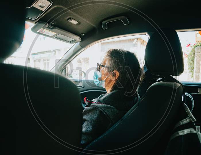 Old Woman With A Mask On In The Front Sea Of A Car