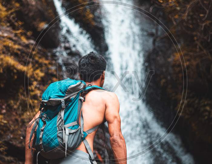 Travel And Freedom. Young Shirtless Boy In Shorts With Rucksack Enjoying Tropical Waterfall View.