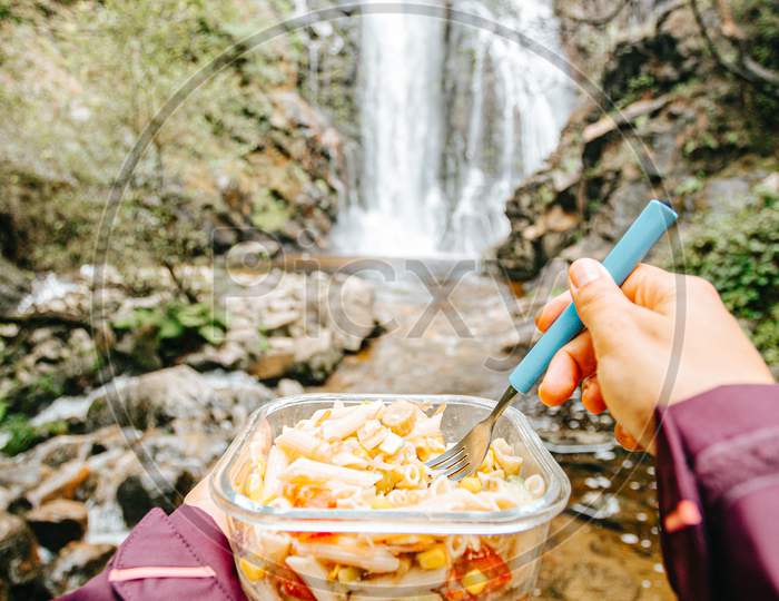 Point Of View Shot Of A Female Hiker Eating In Front Of A Waterfall