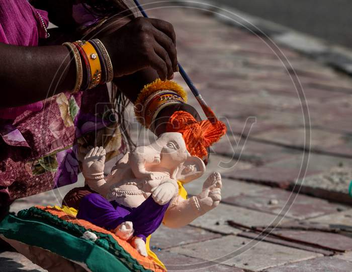 A woman paints an Idol of Ganesha during Ganesh Chaturthi along the roadside in New Delhi on August 22, 2020.