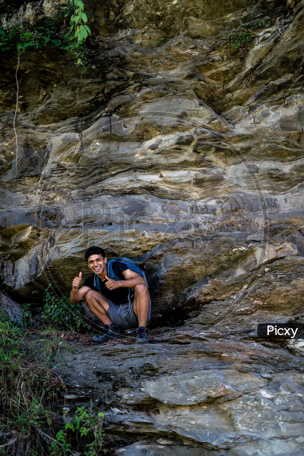 Young Boy Showing Thumbs Up Into The Camera From A Height, After Climbing A Huge Rock.