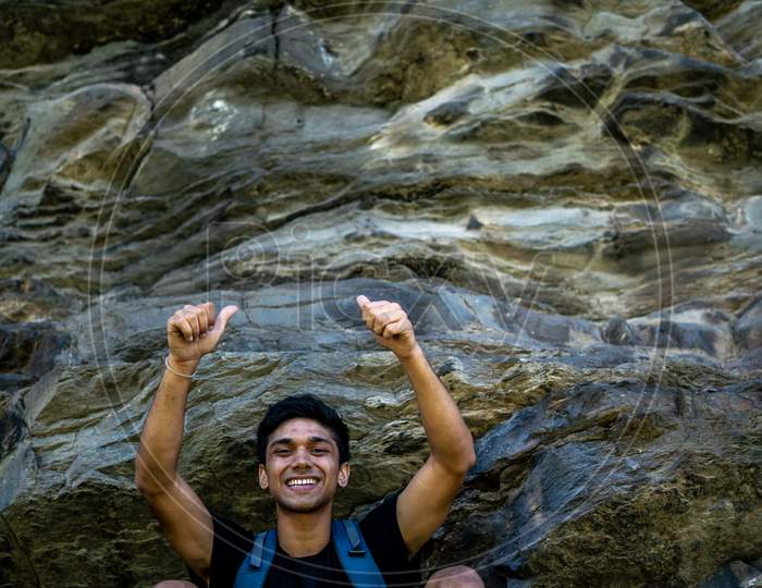Young Boy Showing Thumbs Up Into The Camera From A Height, After Climbing A Huge Rock.