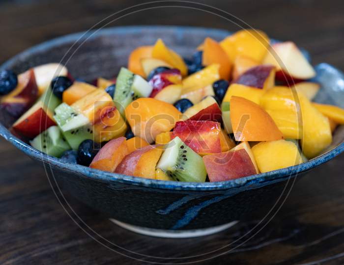 Colorful Fresh Fruit Salad In Dark Bowl On Wooden Table In Daytime