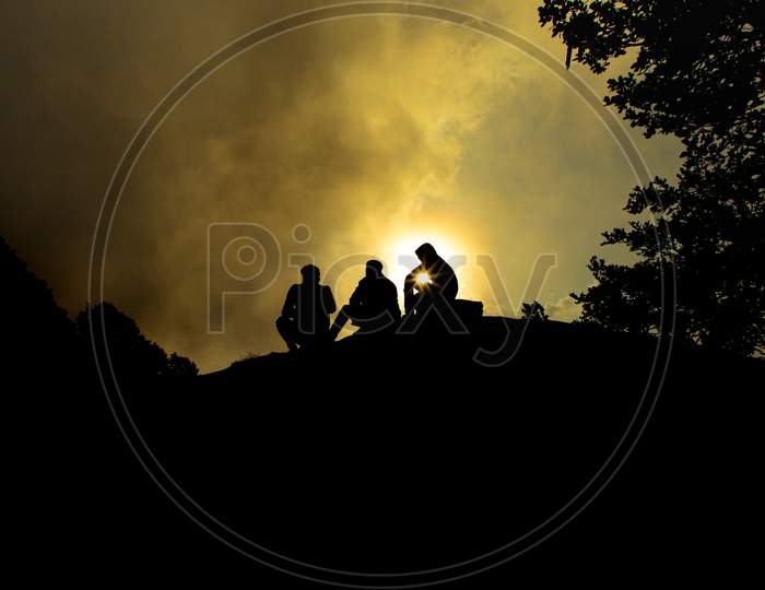 A man is sitting on top of a mountain as the sun sets at hatu peak,himachal pradesh,india.