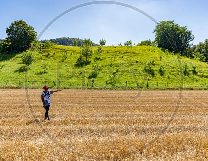 African Woman Showing To The End Of A Golden Harvested Corn Field In Hot Summer Afternoon