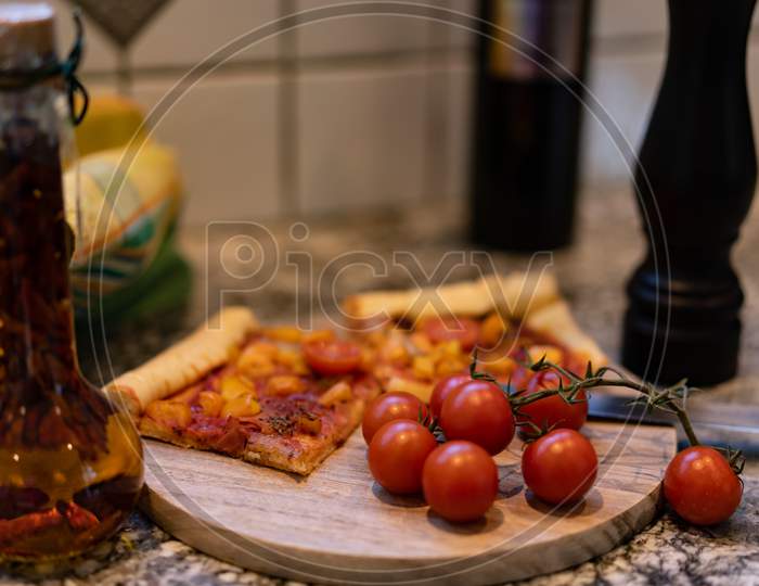 Pizza On A Cutting Board With Fresh Tomatos And Oil And Pepper Mill.