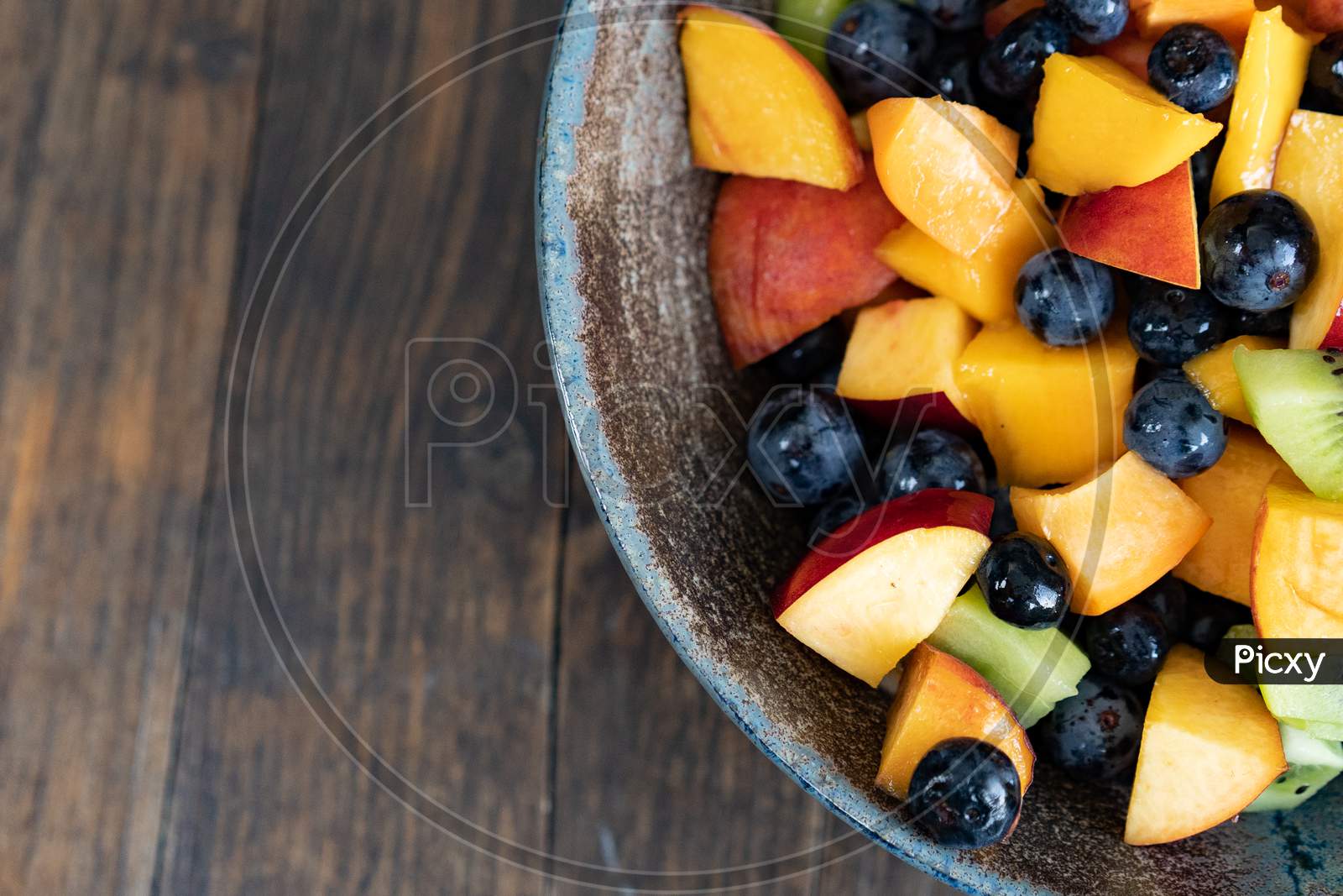 Colorful fresh fruit salad in dark bowl on wooden table in daytime