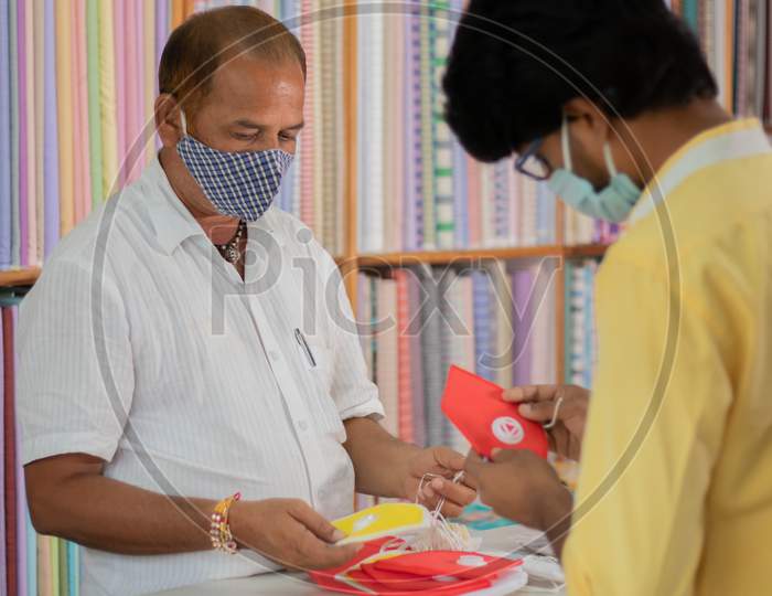 Shopkeeper Selling Masks To Buyer, While Both Wearing Medical Mask To Protect From Coronavirus Or Covid-19 Pandemic - Concept Of Buy Local Or Support Local During Financial Crisis.