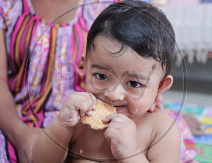 A Newborn Male Toddler Trying To Bite A Biscuit For The First Time With His Gums