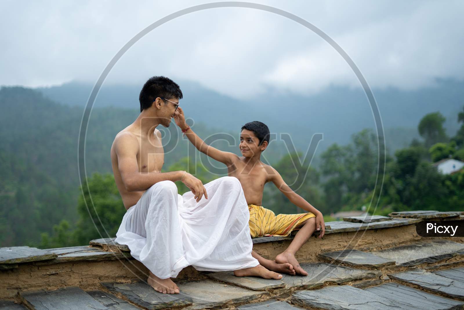 A Young Man Playing With His Younger Brother With Blurred Mountains In The Back.