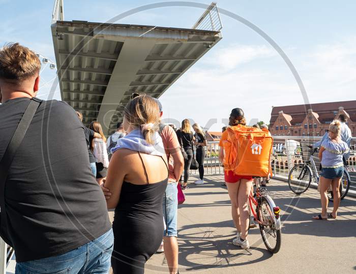 Gdansk, North Poland - August 13, 2020: People Including Essential Food Delivery Worker Awaiting For A Bridge To Connect On Motlawa River During Covid 19 Pandemic Period