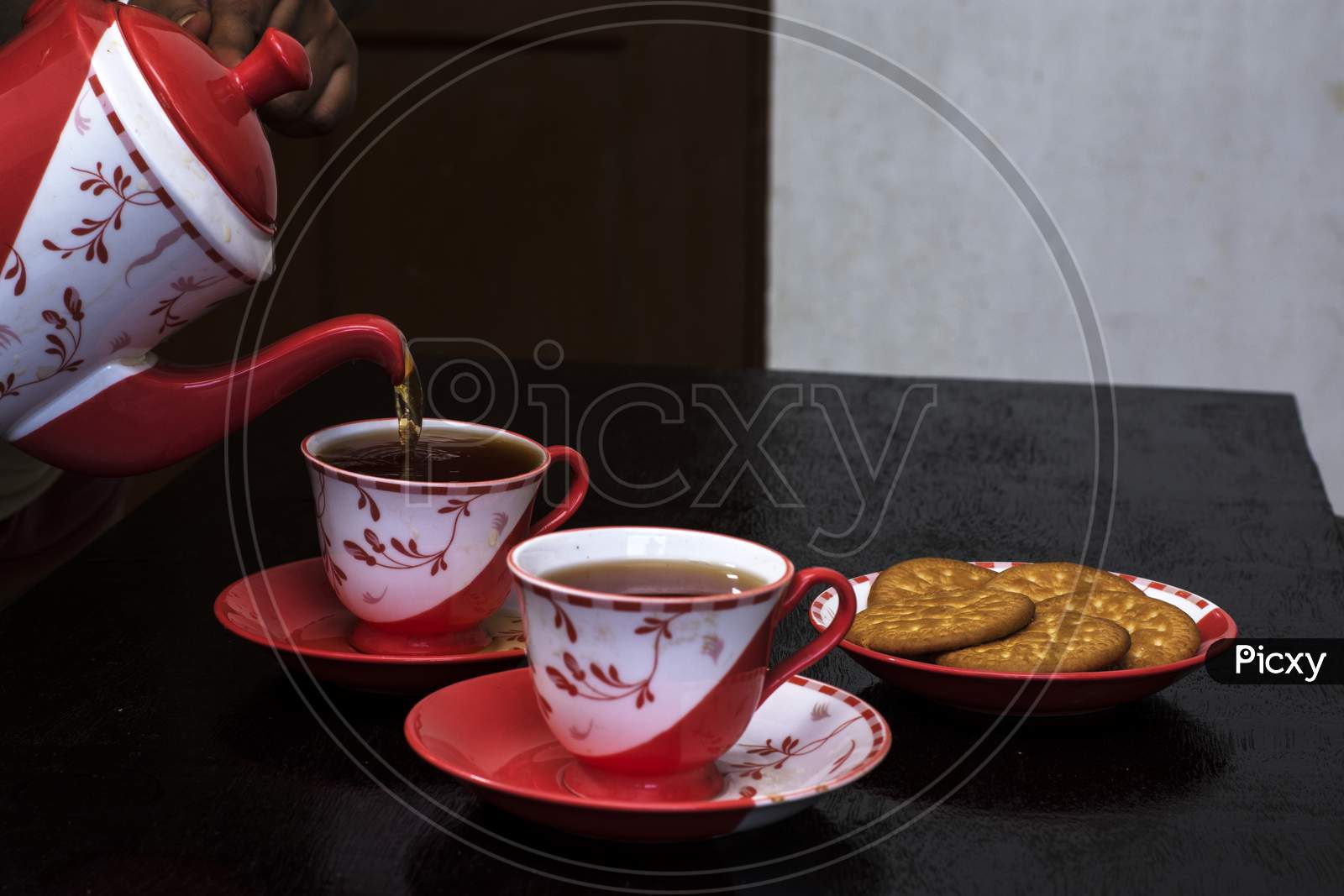 Pouring Tea Into Ceramic Cup On A Wooden Table With Some Biscuit On Plate.