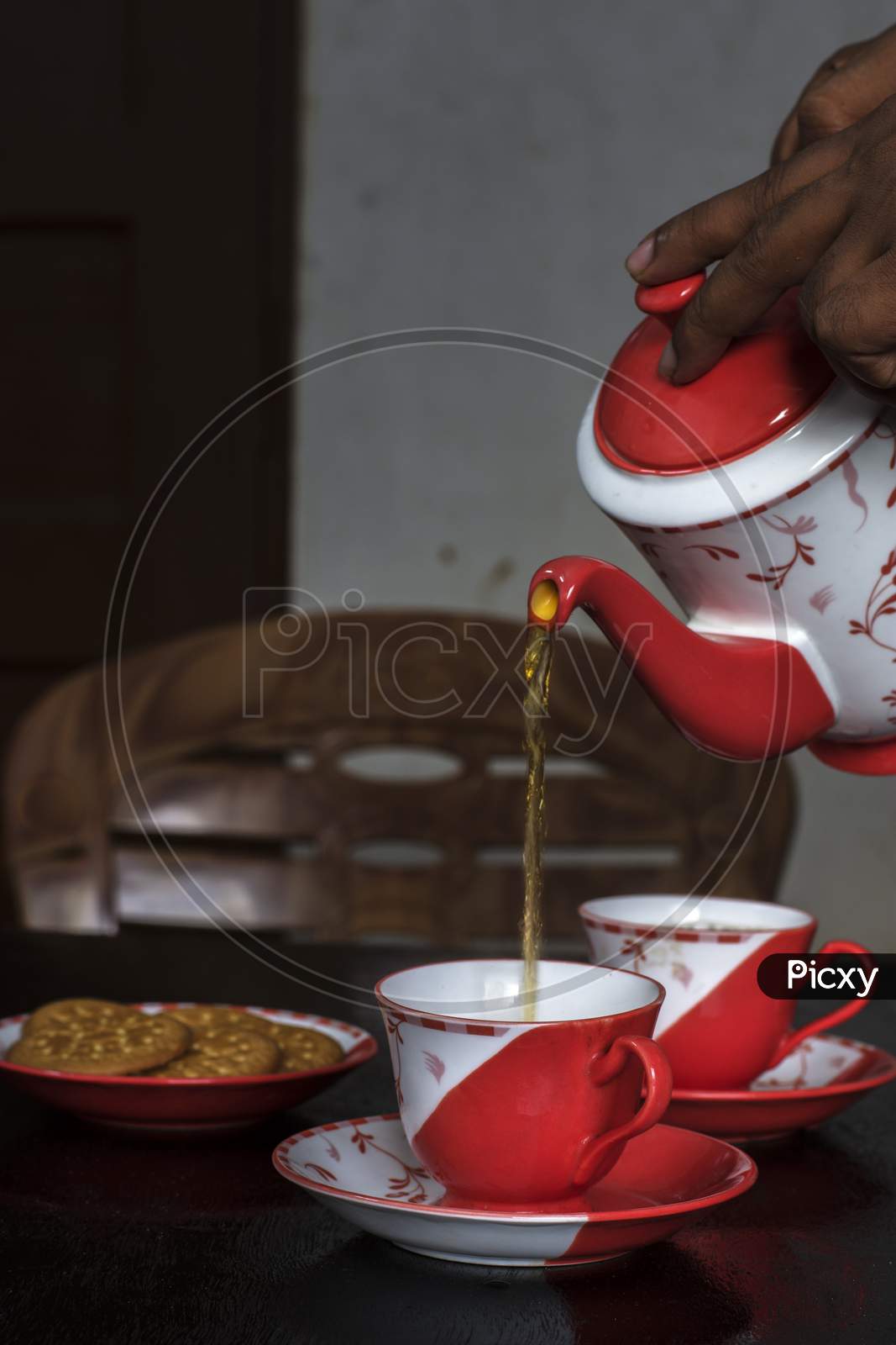 Pouring Tea Into Ceramic Cup On A Wooden Table With Some Biscuit On Plate.