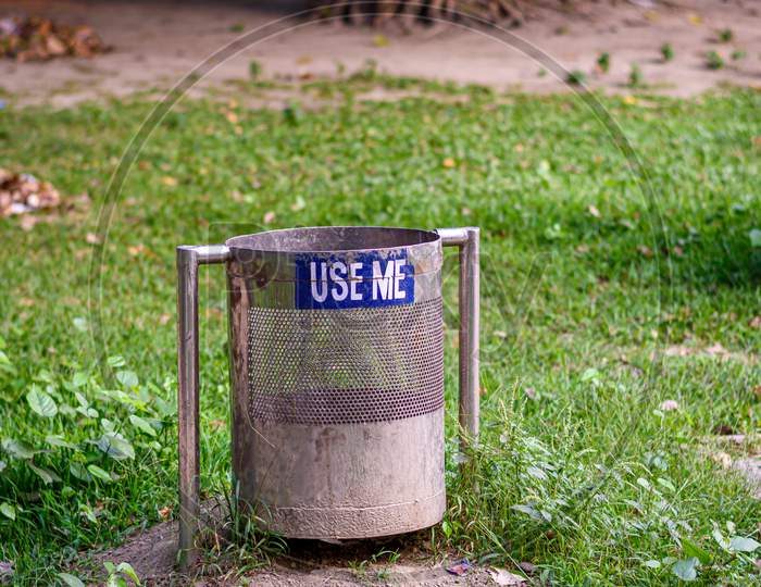 A Picture Of Metallic Dustbin In A Park Beside Lake And "Use Me" Written On It