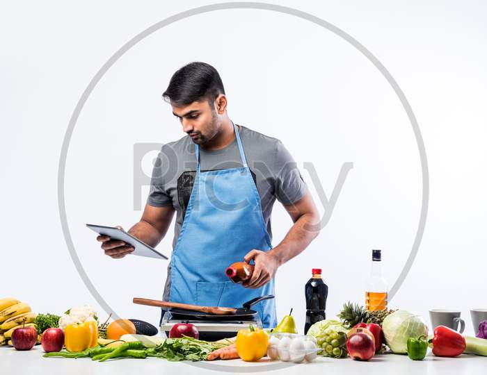 Handsome Indian Man In Kitchen Cooking Food While Wearing Appron