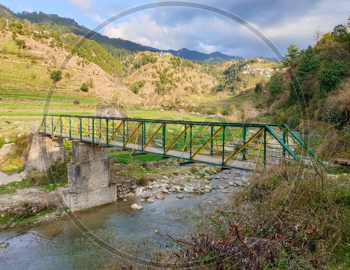 Photo of a steel bridge over a river flowing between beautiful mountains of Himachal Pradesh