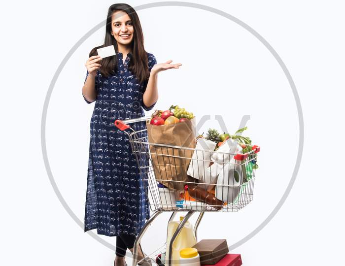 Indian young woman with shopping cart or trolly full of grocery, vegetables and fruits